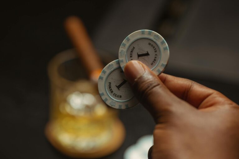 A close-up of a hand holding poker chips with a blurred drink in the background, capturing a casino atmosphere.
